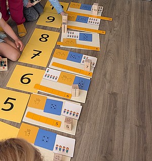 Zahlenkarten und Kinder, die drum herum sitzen und sich mit diesen beschäftigen